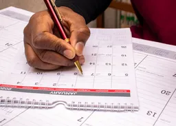 a man's hand writing on a calendar
